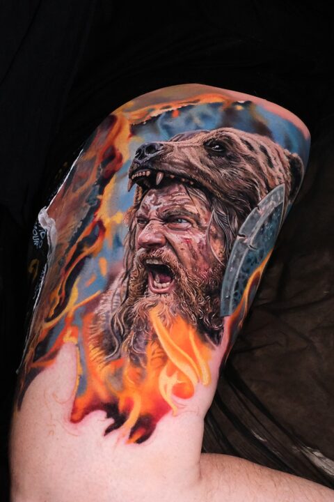 Color realism viking warrior tattoo — bear-pelt hood, roaring berserker, fire and battle axe, thigh sleeve